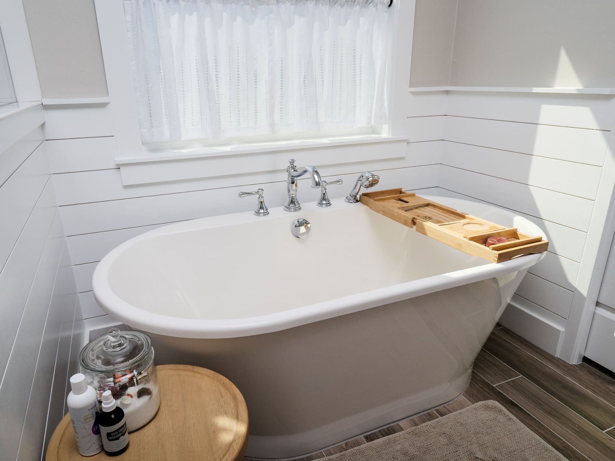 Bathroom remodel with a freestanding bathtub with wood tray in a white-paneled bathroom by Robinson Renovation & Custom Homes in  Gainesville, FL