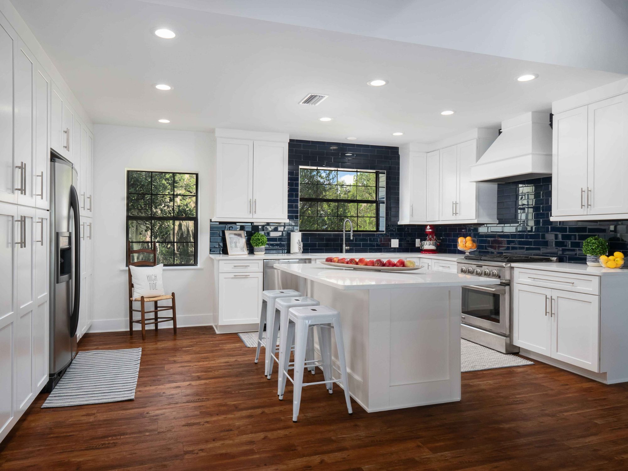 White kitchen in a custom home with a dark blue tile backsplash and an island with seating by Robinson Renovation & Custom Homes in Alachua County, FL